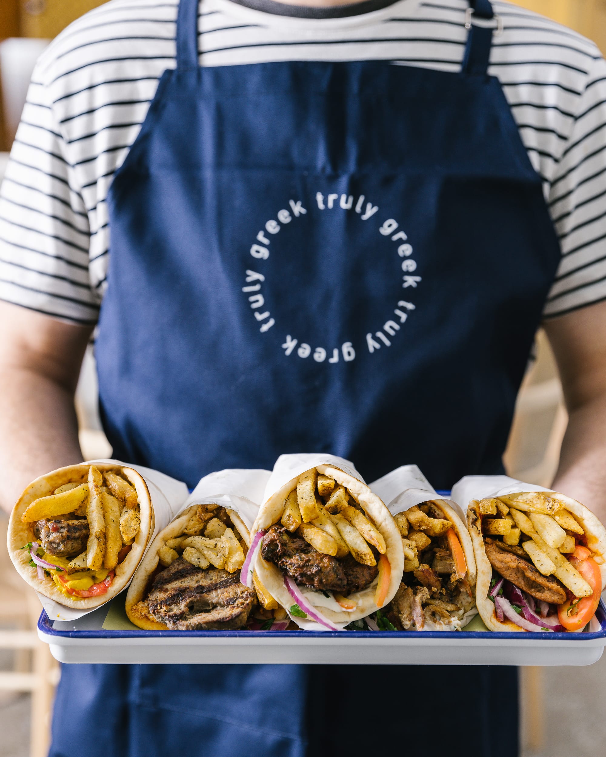 gyros presented on a plate by a person wearing a Greco apron