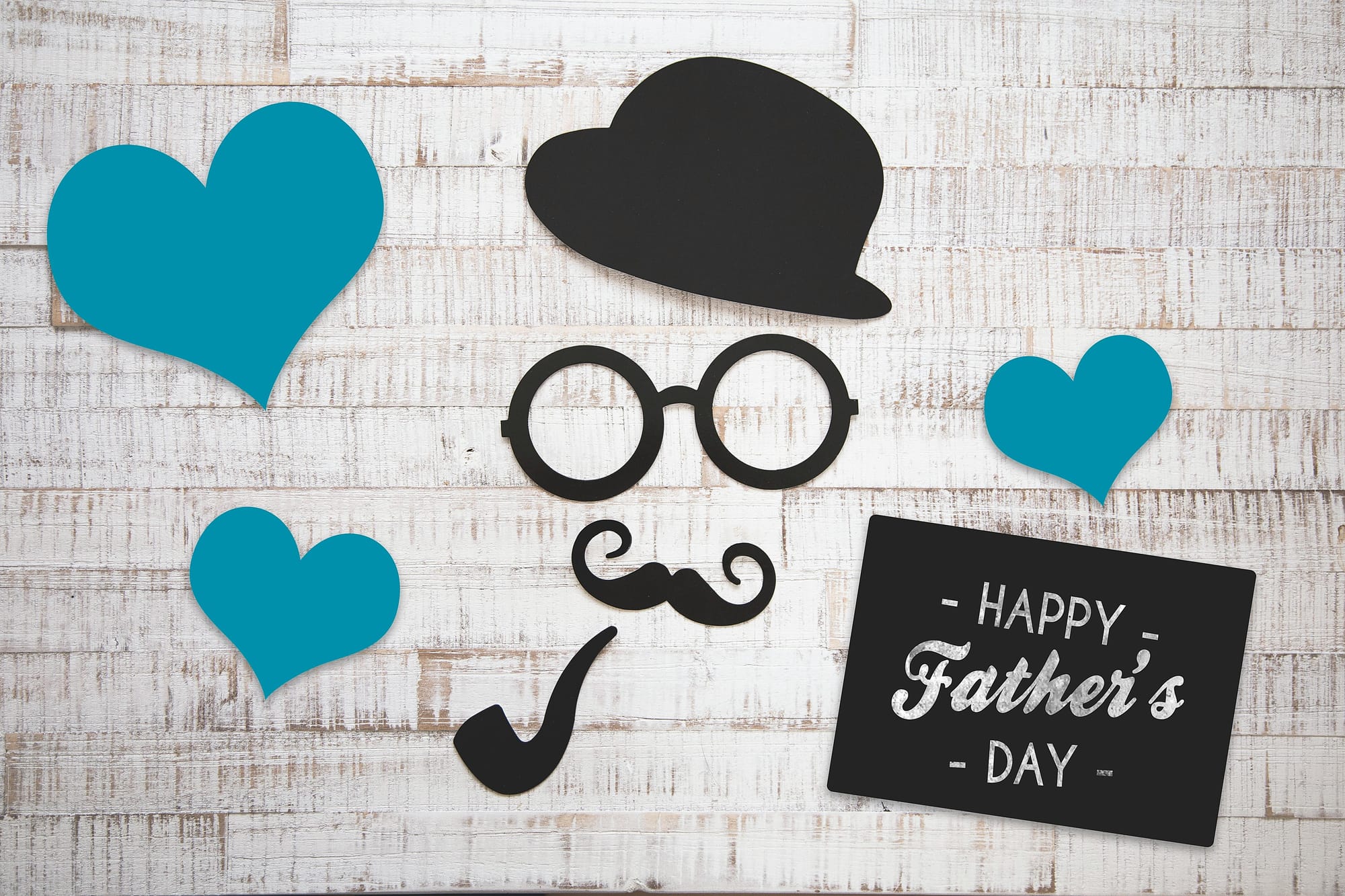 Paper cut out hearts, along with a cut out hat, glasses, mustache, and pipe along with a sign that says, "Happy Father's Day."