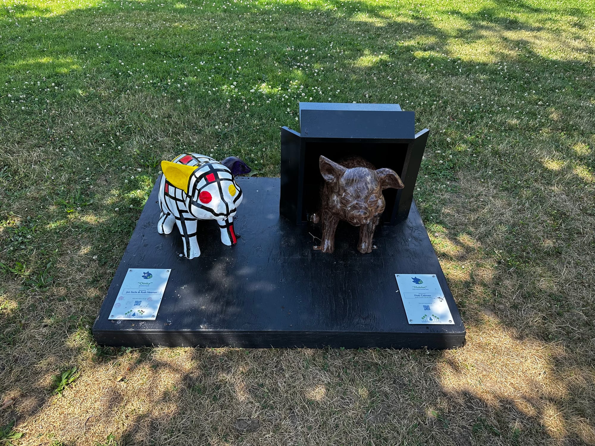 Two small, painted acrylic pigs from the Summer 2024 Pigs on Parade installation on the Burlington, MA, Town Common.