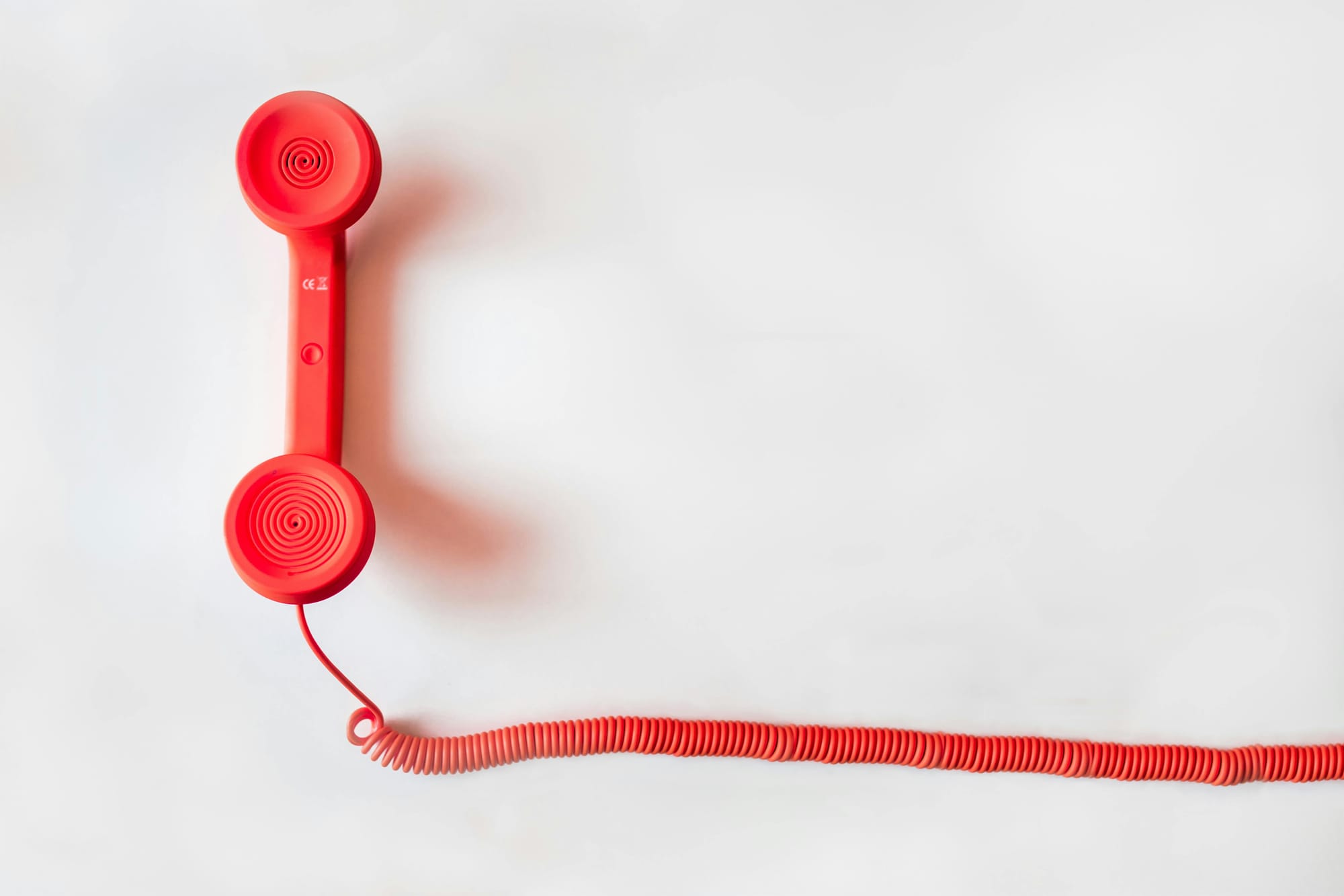 A red corded telephone handset on a white background to represent a call from the emergency alert system.