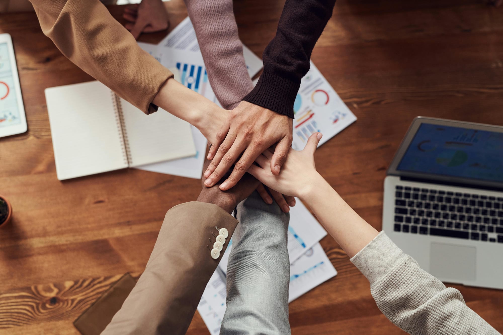 Photo of team members' hands extended toward one another over a wooden table.