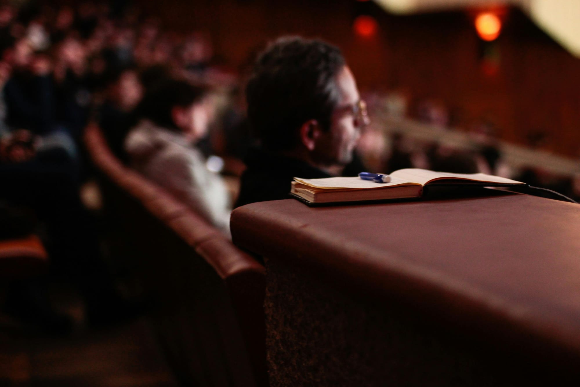 Pen and notebook next to person sitting in auditorium