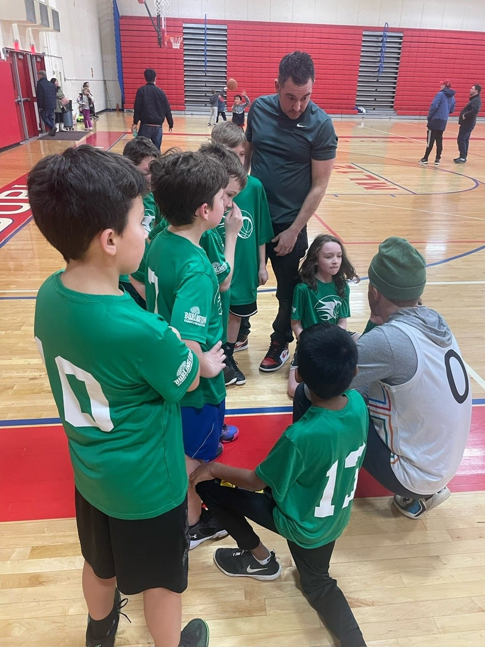 Basketball players talk with their coach in a wood gym