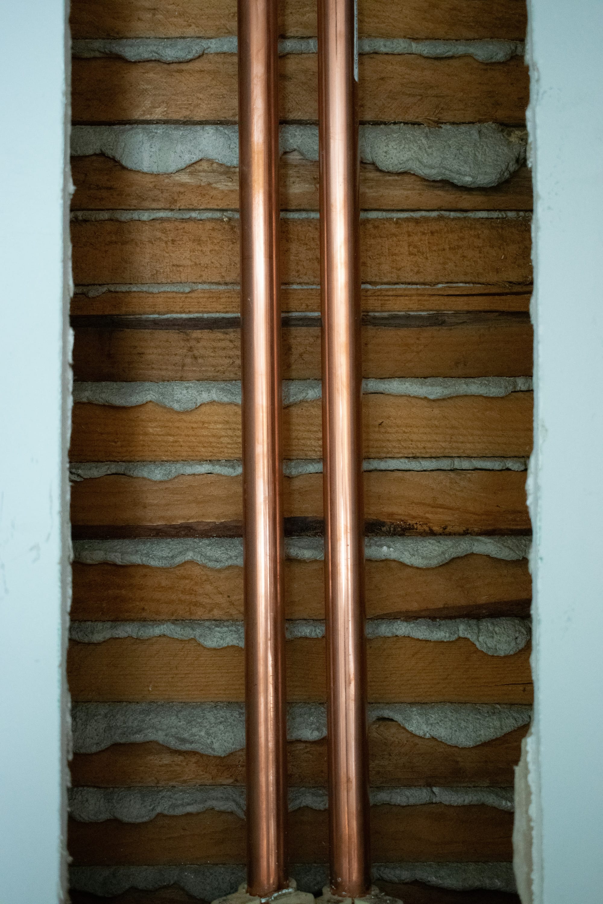 two vertical copper pipes, revealed within a torn away section of a wall